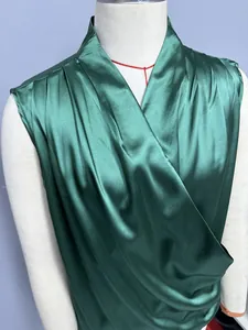 Close-up detail of a dark green satin sleeveless blouse featuring a draped wrap front design