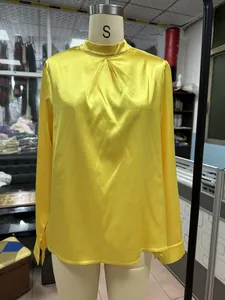 Gelbe Satin-Langarmbluse mit plissiertem Stehkragen in der Detailansicht am Mannequin.