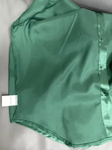 Detail shot of green satin blouse fabric texture and 100% polyester care label tag.