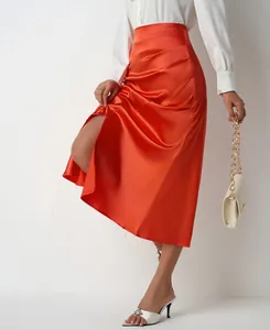 Close-up detail of bright orange high-waisted satin midi skirt with slit and side pleats