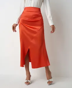 Detail of a bright orange satin high-waisted skirt with pleated accents and a chic front slit.