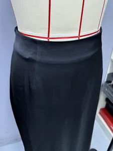 Close-up detail of black satin long skirt showing high waistline and smooth silk-like texture.