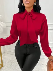 Détail d'un élégant chemisier en satin rouge avec col à nœud papillon et manches longues
