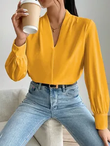 Close-up detail of a bright yellow satin long sleeve blouse featuring a v-neck and pleated cuffs