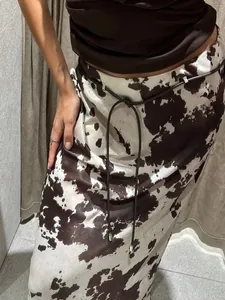 Close-up detail of a cow print satin maxi skirt featuring a slim black cord belt accessory