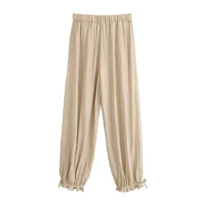 Dettaglio dei pantaloni a lanterna plissettati beige con vita elastica e lacci arricciati.