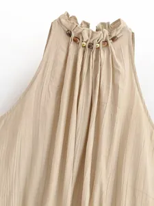 Dettaglio ravvicinato di un top halter plissettato beige con perline in legno naturale.