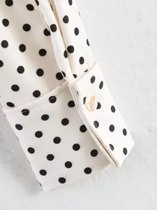 Macro detail shot showing the white fabric with black polka dots and a single button