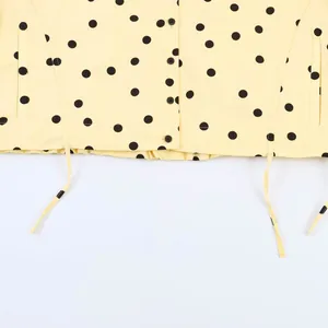 Nahaufnahme des gelben Jackensaums mit Polka-Dots, Kordelzug und schwarzen Knöpfen.
