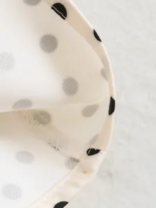 Close-up macro shot of white fabric with black polka dots and fine overlock stitching.
