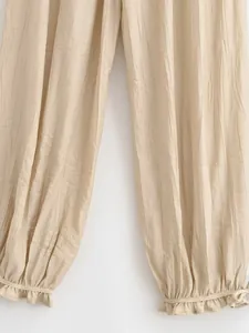 Dettaglio di pantaloni a lanterna beige con texture stropicciata e polsini a volant