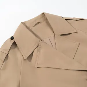 Detailed view of beige trench coat lapels and buttoned epaulets showing fabric texture.