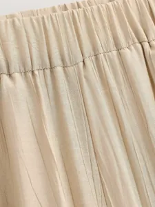 Dettaglio ravvicinato di pantaloni beige a pieghe con elastico in vita e tessuto