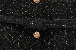 Nahaufnahme von schwarzem Pailletten-Tweed-Stoff mit goldenen Knöpfen und Gürtel