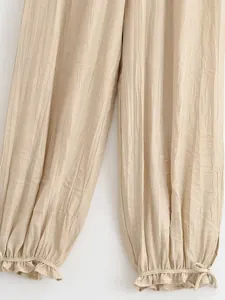 Dettaglio pantaloni a lanterna plissettati beige con fondo a balze e laccetto