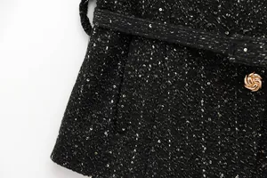 Makrodetail der schwarzen Tweed-Stofftextur mit Goldpailletten und dekorativem Knopf