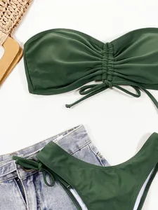 Detailopname van legergroene bikinitop met geplooid trekkoord en denim short plat neergelegd.
