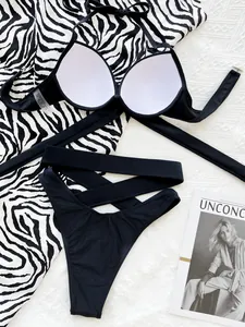 Close-up detail of solid black bikini set with criss-cross waist design and zebra print backdrop