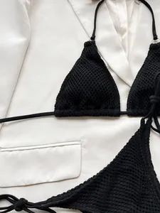 Close-up detail of black crochet bikini top featuring textured mesh fabric on white blazer