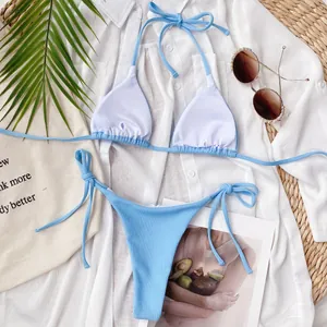 Flat lay of light blue ribbed triangle bikini set on white beach shirt and straw mat