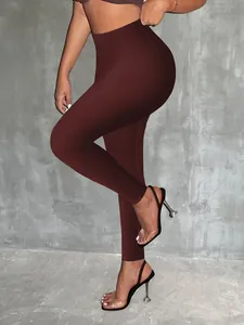 Zij-aanzicht van bordeauxrode leggings met hoge taille en slanke pasvorm tegen betonnen muur