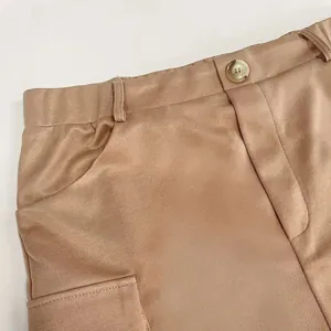 Macro view of the waist button and pocket detail on a khaki knit cargo style skirt.