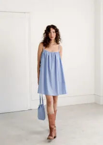 Full body view of a woman in a blue striped sleeveless summer mini dress with brown boots.