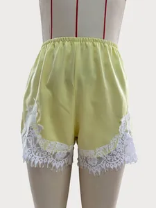 Detail shot of yellow satin shorts featuring elegant white lace trim and scalloped hem.