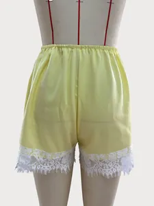 Detailed view of yellow satin shorts featuring elegant white floral lace trim at hem.