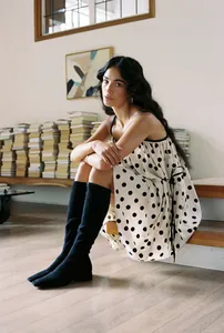 Elegant polka dot summer dress worn by a model sitting on wooden stairs indoors
