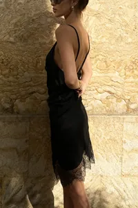 Zijaanzicht van een zwarte satijnen slipdress met elegante kanten bies aan de zoom.