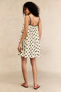 Back view of a chic cream mini dress featuring black polka dots and thin spaghetti straps.