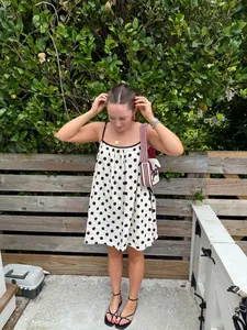 Lifestyle detail shot of a woman wearing a white polka dot summer dress with black trim