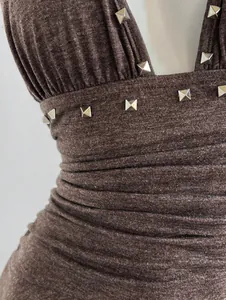 Detalle de vestido halter marrón con tachuelas metálicas plateadas y textura de punto.