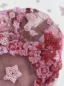 Gros plan sur une broderie de paillettes florales roses sur un tissu de dentelle fin