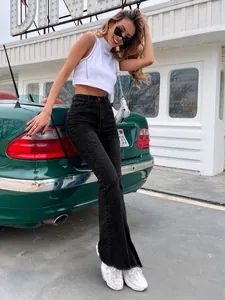 Model in zwarte flared jeans met hoge taille en rafelige zoom naast een groene auto