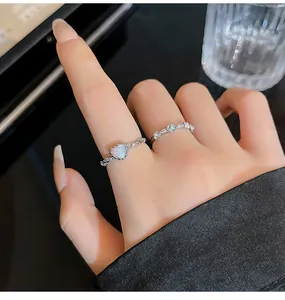 Exquisite Nahaufnahme eines silbernen Herz-Opal-Rings und eines Blumenbandes an einem Finger