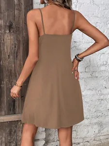 Back view of a brown solid color spaghetti strap mini dress with a rustic wall background