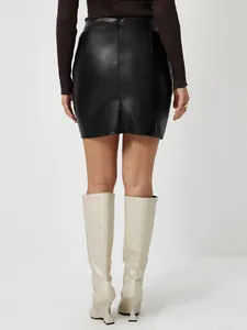Vue arrière d'une mini-jupe en similicuir noir à taille haute avec des bottes crème élégantes