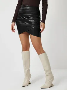 Détail d'une mini-jupe portefeuille en similicuir noir avec fronces et coupe ajustée