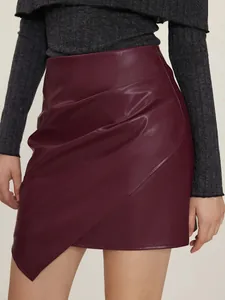 Close-up detail of burgundy PU leather skirt featuring an asymmetrical draped hem and high waist.
