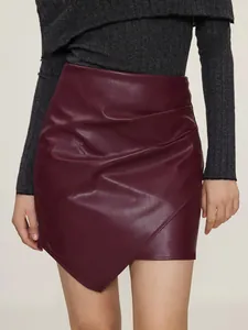 Detailed macro view showing texture of wine red PU leather mini skirt with pleated asymmetric hem