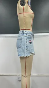 Dettaglio di shorts in denim azzurro a vita alta con orlo sfilacciato e toppa ricamata