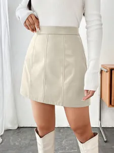 Détail d'une mini-jupe trapèze en similicuir beige avec des coutures verticales.
