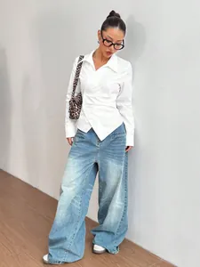Dettaglio di una donna che indossa una camicia bianca asimmetrica e jeans larghi