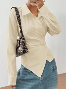 Dettaglio di una camicetta beige a maniche lunghe con orlo irregolare e bottoni.