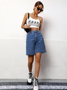 Full body view of model wearing relaxed blue denim bermuda shorts against a white wall