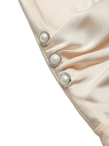 Detail view of champagne satin fabric with decorative pearl buttons on an elegant bodysuit