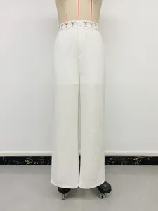Dettaglio dei pantaloni bianchi a gamba larga con pizzo in vita e texture stropicciata