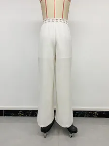 Dettaglio di pantaloni bianchi a gamba larga con elegante pizzo traforato in vita.